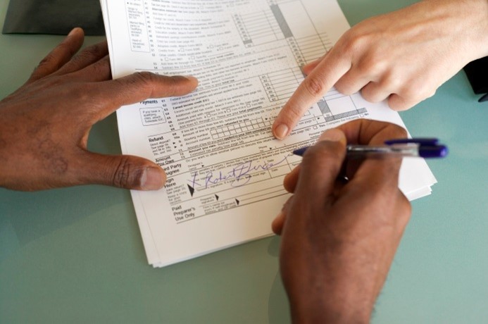 This is a picture of a person filling in a form and and another person indicating where to sign the form.