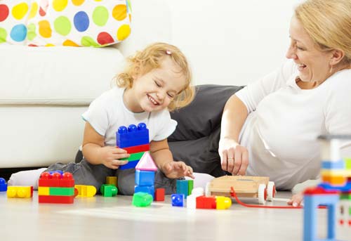 A woman and a little girl, sitting on the floor playing with blocks.