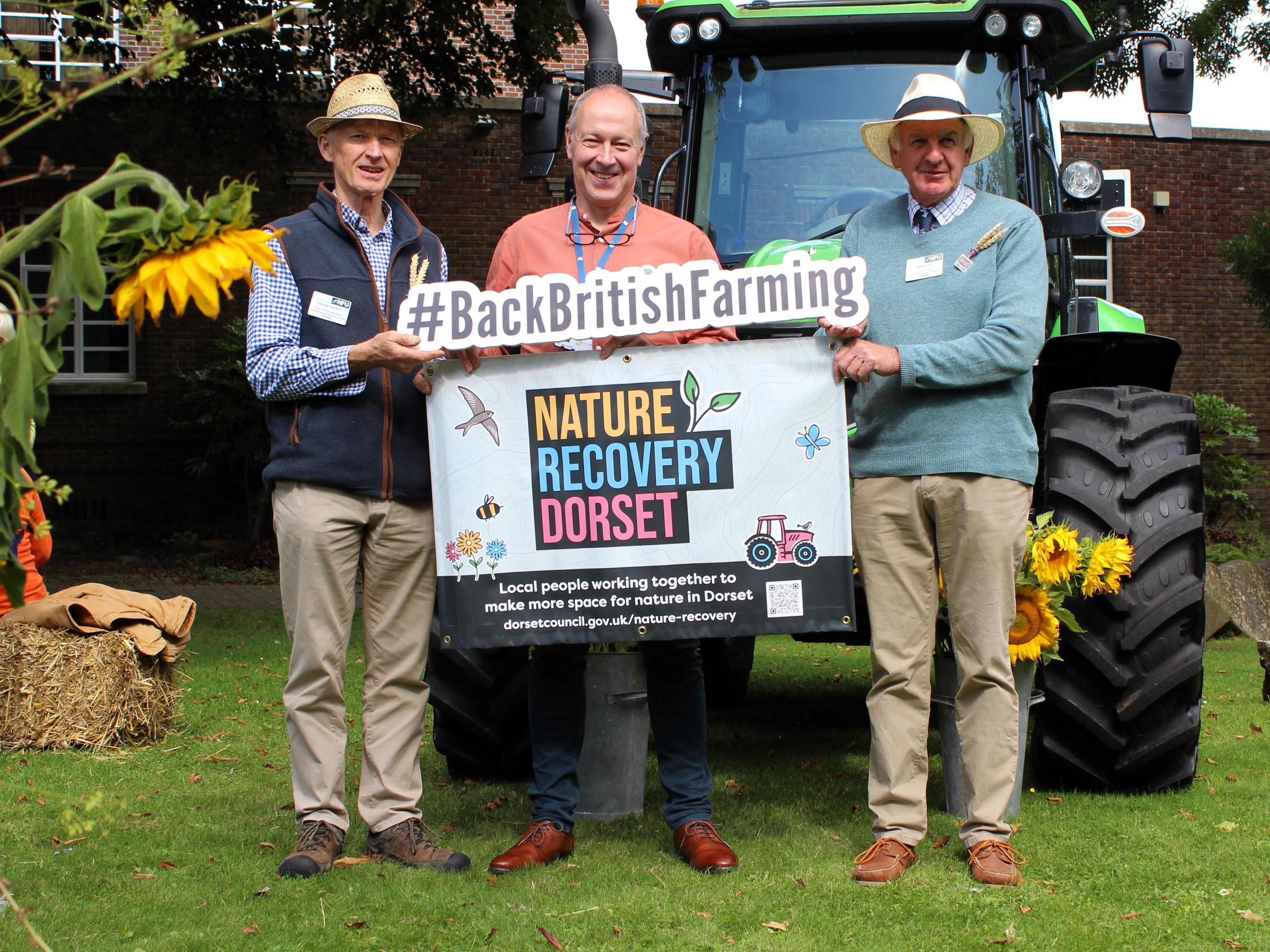 three individuals pose for picture in front of tractor holding &#39;Nature Recovery Dorset&#39; and &#39;Back British Farming&#39; signs