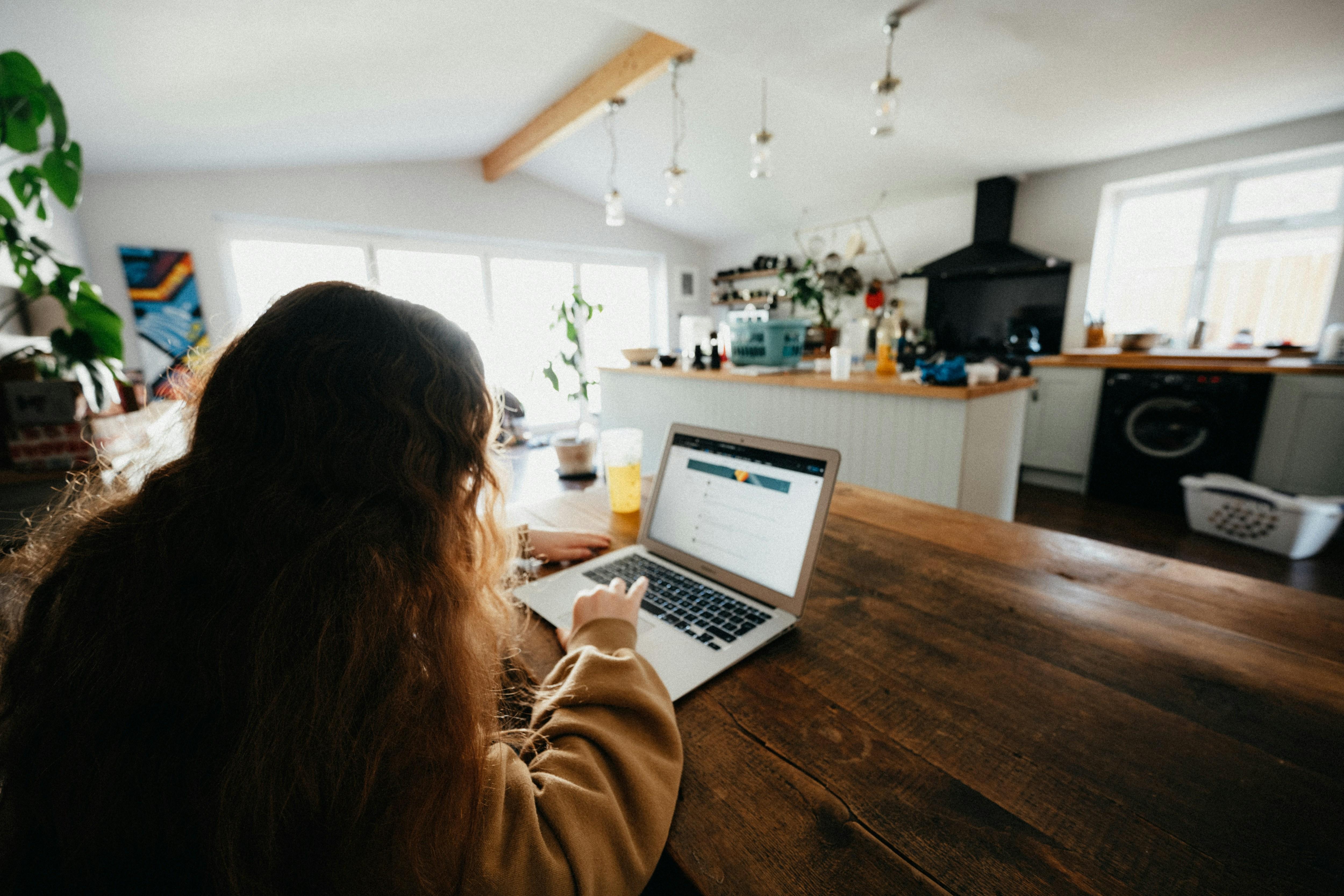 teenage girl using a laptop at the kitchen table with a view of the kitchen in the background