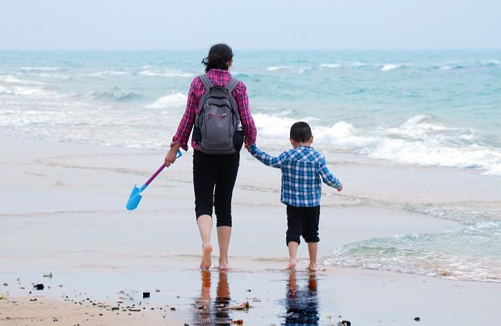 a woman is walking on a Dorset beach and holding the hand of little boy. They are paddling.