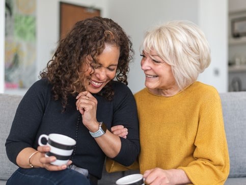 Two people on a sofa holding coffee cups and laughing together