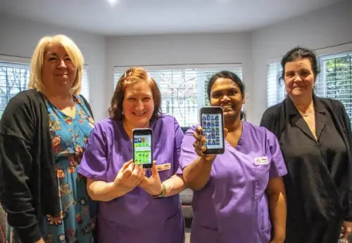 4 people standing together. 2 people in the middle showing their phone screen.