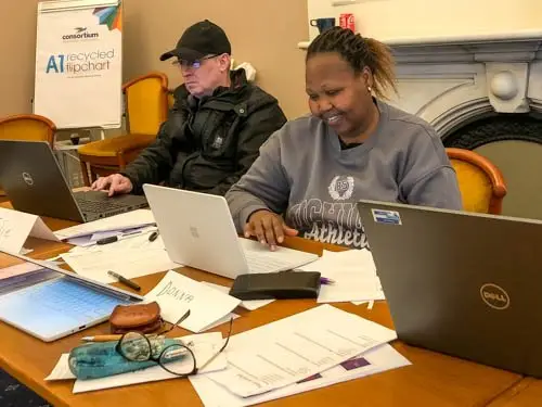 Two people sitting on a desk, in front of their laptop