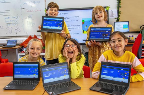 5 children, 4 girls and a boy holding laptops with coding activities on the front of them