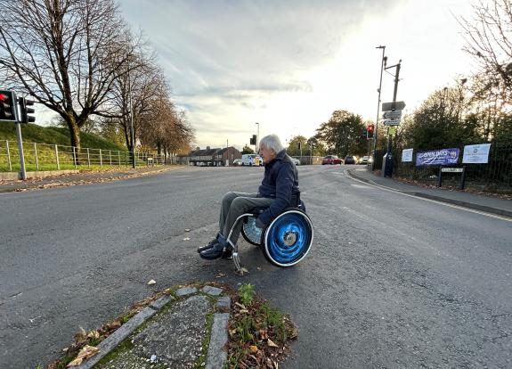 A man seated in a wheelchair waiting to cross a road